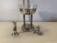 Silver decor set on a beige table: Aris 900 vase/candle holder, Argentor bowl and deer figurine