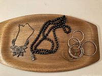 Photo of entire lot showing the floral necklace, black beaded necklace with Buddha pendant, and multiple metal bangles on a wooden tray.