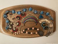 Wide shot of entire collection of vintage ethnic jewelry laid on wooden board, showing several pieces including belt, necklaces, earrings, and brooch.