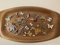 Top-down image of wooden tray displaying about 30 various vintage butterfly pins and brooches in multiple colors and styles.