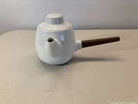 Front profile view of white porcelain teapot with teak handle