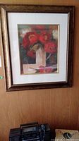 Photo of the framed print showing the entire artwork with red flowers in a vase, wood panel wall background.