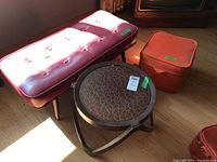 Photo showing burgundy vinyl bench with button tufting, plastic outdoor table with round mottled brown cracked top, and rust-colored square vinyl ottoman, all with noted wear and vinyl splitting.