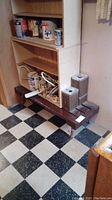 Dark stained wood bench with a simple rectangular top placed beside a shelving unit in a basement with checkered black and white tile floor.
