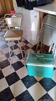 Overall view showing bar stool next to vintage green Coleman cooler on checkered floor.