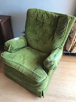 Front angle of vintage green upholstered rocker chair showing cushioned arms and backrest with fabric wear.