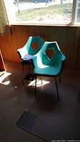 Pair of molded resin chairs placed near window showing color and shape with hexagonal cutout backs and metal legs.