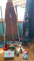 Cleaning items including vintage wooden ironing board with floral design, two GE irons, multiple mops and brooms, Johnson & Johnson first aid kit.