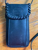 Photo showing black leather Rugged Gear phone case with stitched edges and embossed logo on wooden surface