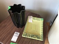 Two pieces of pottery on a wooden surface. Left is a black Beauceware pottery vase with a star-shaped wavy rim. Right is a square green and yellow mottled pottery ashtray with a stepped concentric square design.