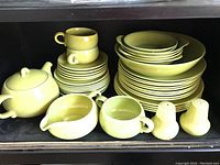 Photo showing stacked platters, plates and cups alongside salt and pepper shakers, sugar bowl, sauce boat in green ceramic.