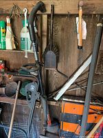 Photo of the edge trimmer, garden shovel, and lawn mower hung on wooden shed wall with surrounding garden chemicals and tools.