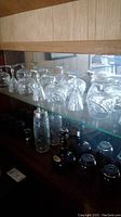 Shelves with various clear glassware including stemmed glasses, tumblers with etched patterns, and a cocktail shaker with metal top.