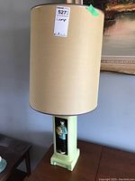 Full view of the lamp showing the cylindrical fabric shade and pale yellowish-green ceramic base with rectangular cutout.