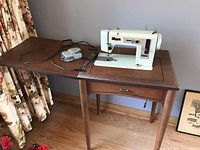 Vintage Simpsons sewing machine attached to wooden table with drawer. Includes power cord and foot pedal.