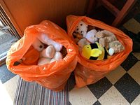 Two large orange bags filled with assorted stuffed animal toys seen from above and the side, showing a variety of animals inside.