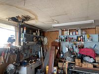 Wide angle photo of workshop corner showing pegboards with hand tools and shelves with supplies and cans
