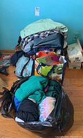 Photo of clothing piles including jeans, sweaters, scarves, and bags packed with clothes.
