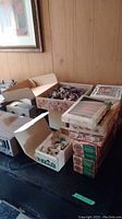 Photo showing multiple boxes of vintage Christmas decorations and ornaments on a table.