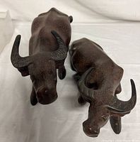 Front view of two carved water buffalo sculptures showing the standing and recumbent poses with textured fur and curved horns.