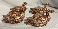 Four ceramic mallard duck trinket boxes arranged on a gray surface, showing detailed feather texture and overall shape.