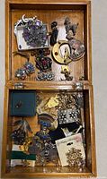 Top view of wooden box with varied vintage brooches and pins including crescent moon with rhinestones, animal shapes, and floral designs.