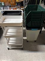Photo shows white and black rolling carts with three baskets each and four stacked green baskets inside recycling bin.