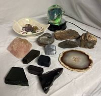 Wide view of the mixed lot showing natural rocks, geodes, agate slice, and colored glass pieces on a reflective white background