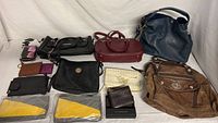 Collection of handbags and wallets arranged on a white surface showing variety in color, size and style including leather and canvas.