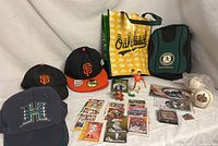 Display of mixed sports memorabilia including several baseball caps, sports cards, figurines, signed baseballs, and branded bags