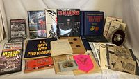 Overview of collection showing multiple military books, DVDs, vintage documents, certificates, and a US Marine Corps belt buckle.