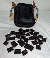 Black leather drawstring bag standing with leather rune tiles laid in front showing runic symbols.
