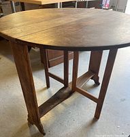 Full view of the wooden round drop leaf table showing legs and folded configuration.