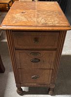 Front view of wooden side table with three drawers and brass handles, showing decorative wood carving and wear on drawer fronts.