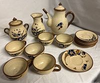 Full set arranged on white surface displaying teapot, creamer, sugar bowl, cups, bowls, and saucers.