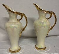 Pair of vintage pearl opalescent pitcher vases with 22kt gold handles, shown together on a white surface.