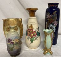 Group photo of five vases showing different styles and sizes, includes blue Kutani cobalt vase with bird, gold hand-colored vase with floral scene, white tapestry textured vase with flowers, mint green vase with gold accents, and wooden vase.
