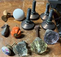 Overview photo showing all items including various vintage glass, porcelain, and ceramic door knobs, a brass propeller, and metal foot levelers on a wooden surface.
