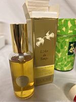 L'Air du Temps perfume bottle with original gold box and green patterned container in background.