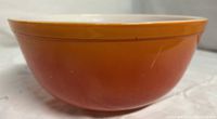 Side view showing the orange exterior of the vintage Pyrex mixing bowl on a soft white background.