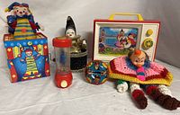 Full view of six clown-themed vintage toys including Fisher Price music box TV, crocheted clown doll, red toy with beads, tin clown jack-in-the-box, small clown toy in glittery box.