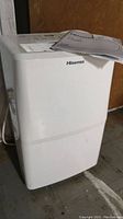 Front side view of white Hisense dehumidifier with manual placed on top.