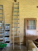 Full view of the aluminum extension ladder leaning against a brick wall, showing its height approximately extended to near full length.