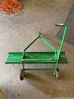 Top view of the green metal John Deere TA-400JD dethatcher with yellow wheels and handle attachment.