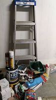 Full view of 4-foot Lite Grade 3 aluminum step ladder with blue plastic top tray standing against white wall alongside various painting supplies arranged at its base on concrete floor.