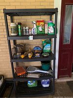 Front view of black collapsible plastic shelving unit with five shelves. Shelves are slatted and the unit is assembled. Used for gardening supplies but contents are not included.