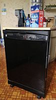 Front view of portable dishwasher, black with woodgrain laminate top. Control panel on front.