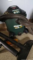 Front view of green and black Shop Vac with hose attached showing capacity and peak horsepower.