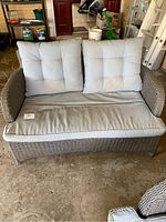 Front view of outdoor rattan lounge chair with grey cushions placed on a concrete surface indoors.