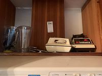 Photo showing the full set of appliances on a shelf: the Osterizer blender base with jar and pitcher, white hand mixer with beaters placed on the side.